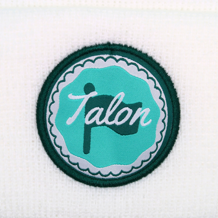 White Knit Beanie with Green and Teal Circle Logo Closeup.