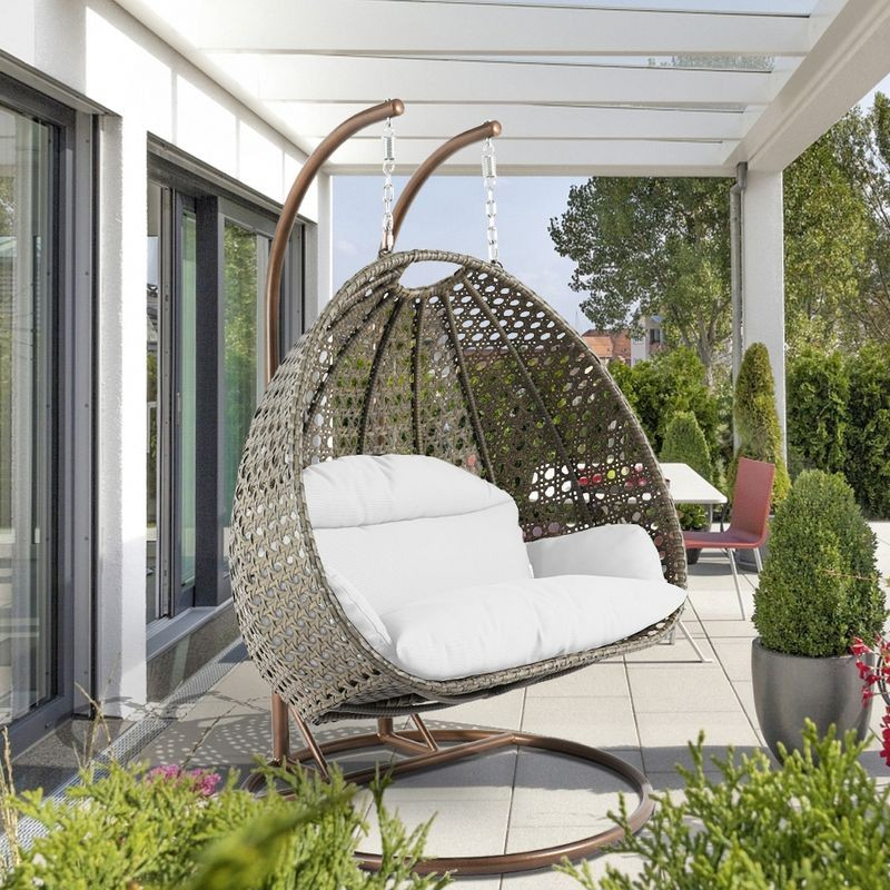 LeisureMod Beige Wicker Hanging 2 person Egg Swing Chair White on Patio.