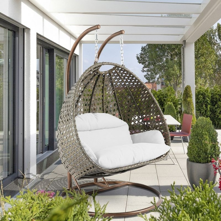 LeisureMod Beige Wicker Hanging 2 person Egg Swing Chair White on Patio.