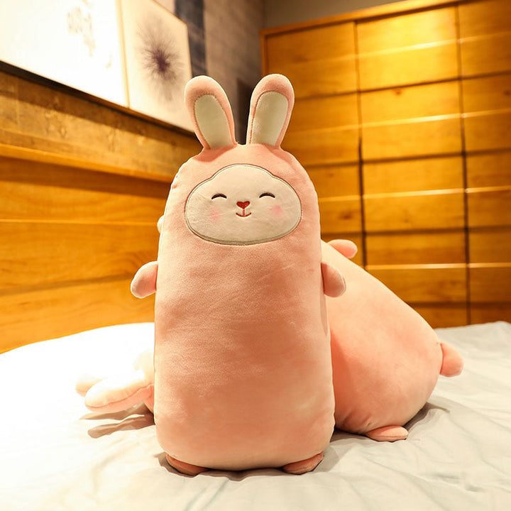 Pink plush toy shaped like a rabbit on a bed with wooden paneling in the background.