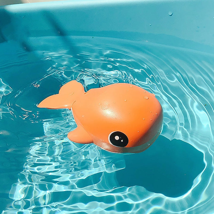Orange toy whale floating in clear blue water.