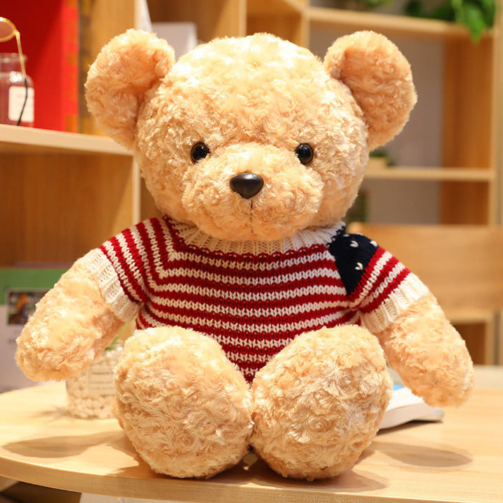 Plush teddy bear wearing a red, white, and blue striped sweater on a wooden surface.