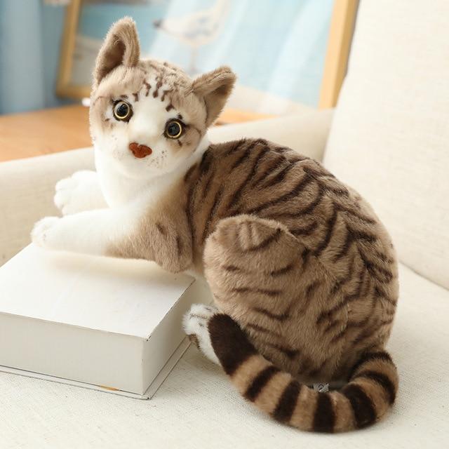 Plush toy cat with brown and black stripes sitting on a white surface.