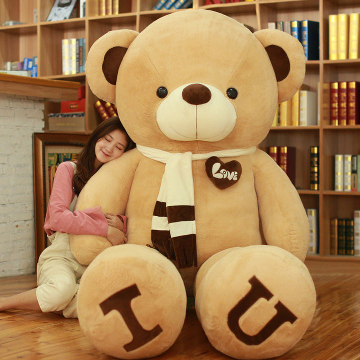 Large teddy bear with I U on its feet and a person hugging it in a room with bookshelves.