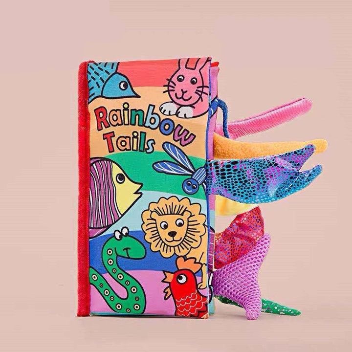 Colorful children's book titled Rainbow Tails with fabric tails attached on a beige background.