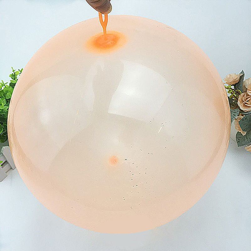 Large transparent balloon with a small orange object inside, held by a hand against a light background.