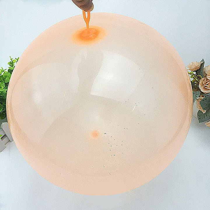 Large transparent balloon with a small orange object inside, held by a hand against a light background.