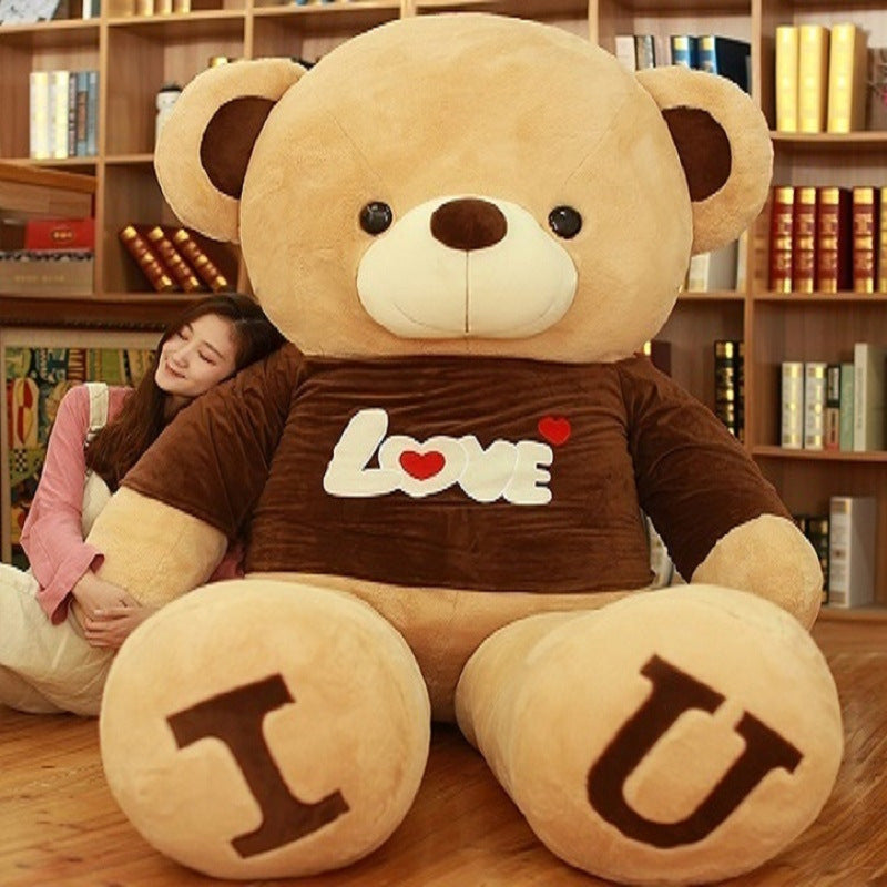 Large teddy bear with I U on its feet and a person hugging it in a room with bookshelves.