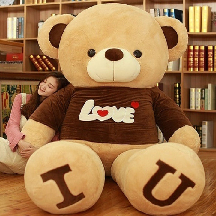 Large teddy bear with I U on its feet and a person hugging it in a room with bookshelves.