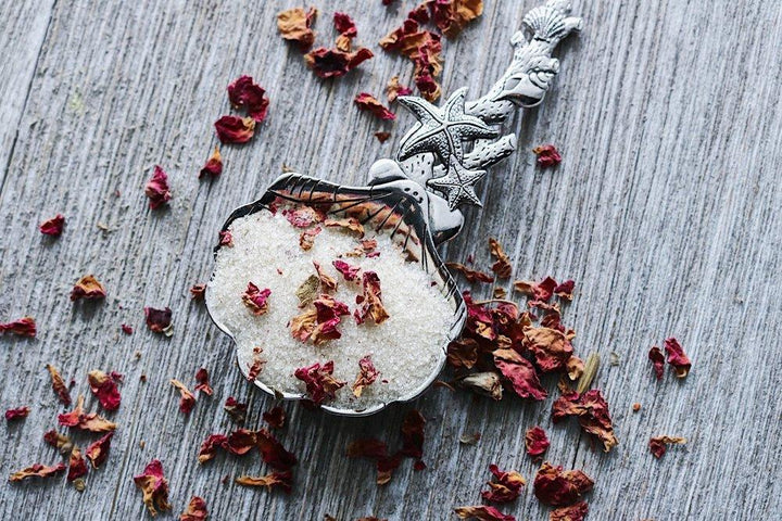Decorative spoon with sugar and dried flowers on a textured surface.