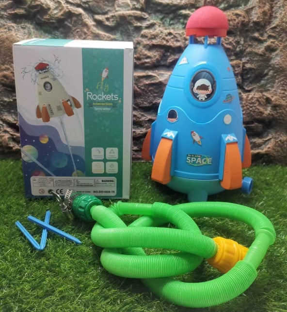 Toy rocket with hose on grass next to its packaging.