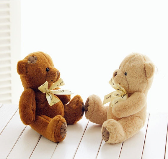 Two teddy bears holding hands on a wooden floor with a white background.