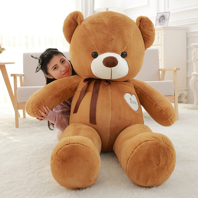 Large brown teddy bear with a heart tag, held by a person in a bright room.