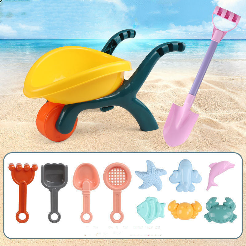 Colorful sand toys including a wheelbarrow, shovel, and various molds on a sandy beach background.