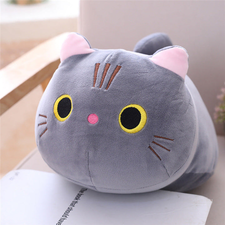Plush cat-shaped pillow on a surface with a blurred background.