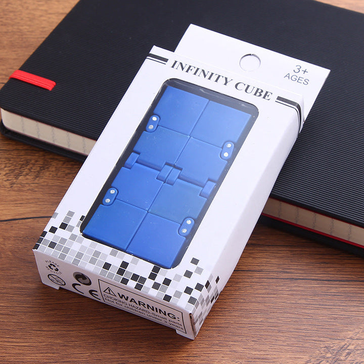 Box of Infinity Cube toy on a wooden surface with books in the background.
