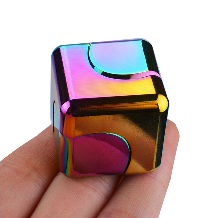 Multicolored metallic cube held in a hand against a white background.