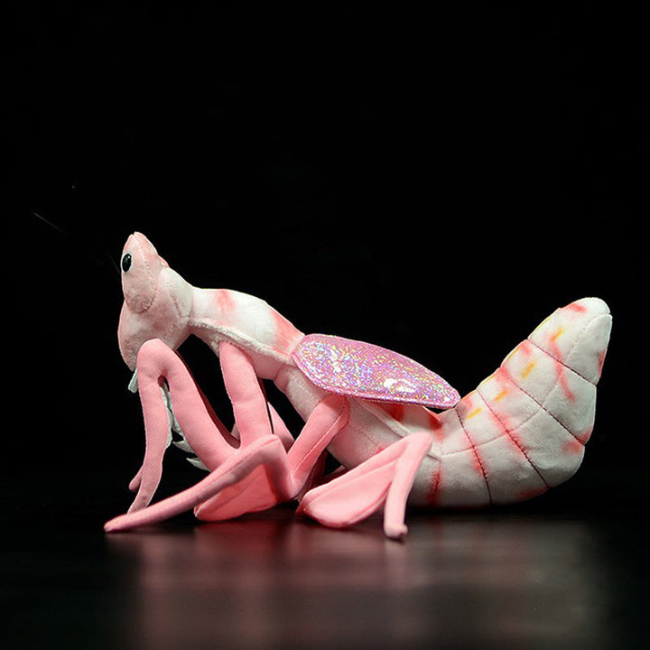 Plush toy resembling a praying mantis with pink and white colors on a black background.