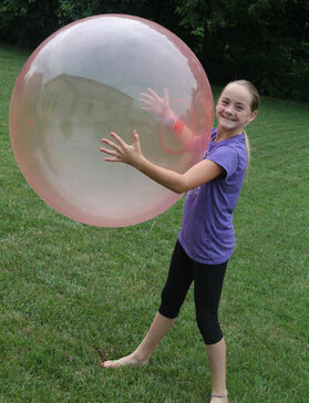 Person holding a large transparent bubble ball on grass.