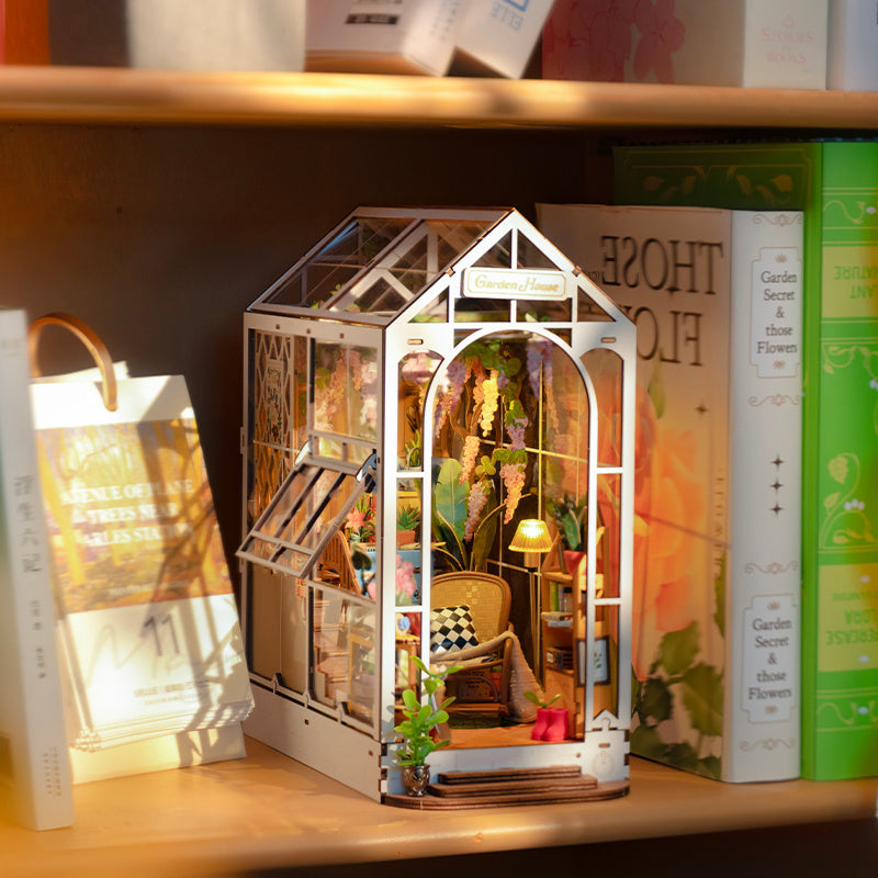 Miniature model of a greenhouse on a bookshelf with books around.