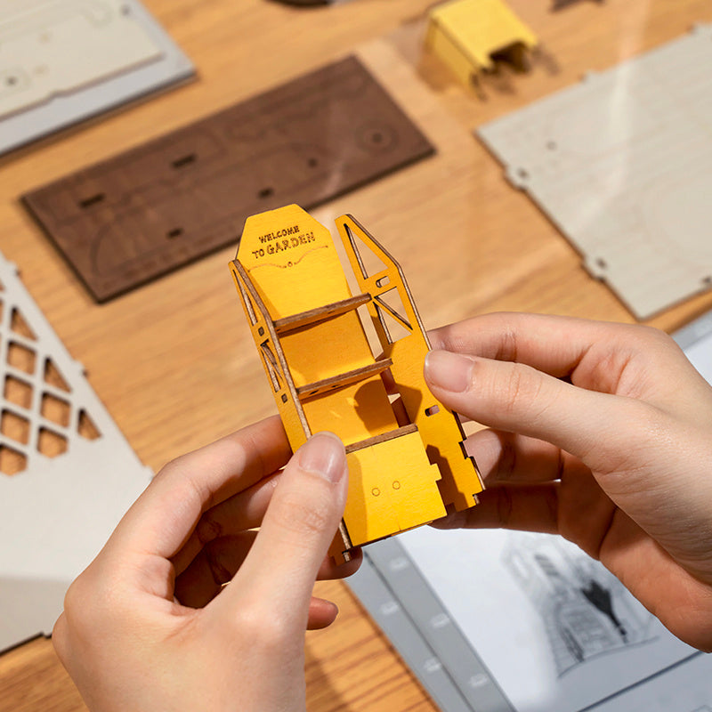 Person assembling a yellow 3D puzzle on a wooden table.
