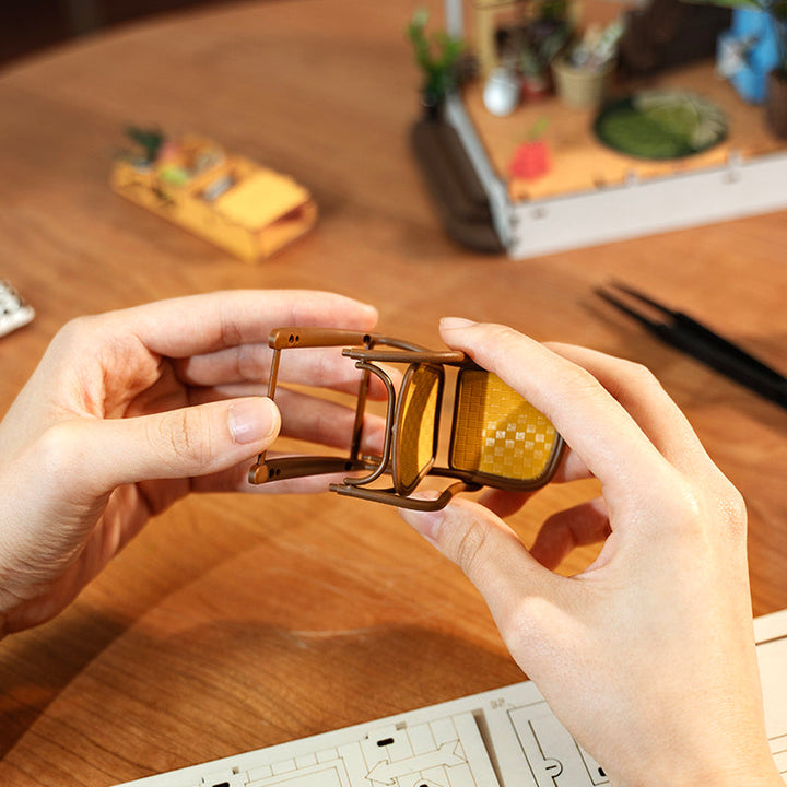 Person holding a small metallic object on a wooden table with blurred background.