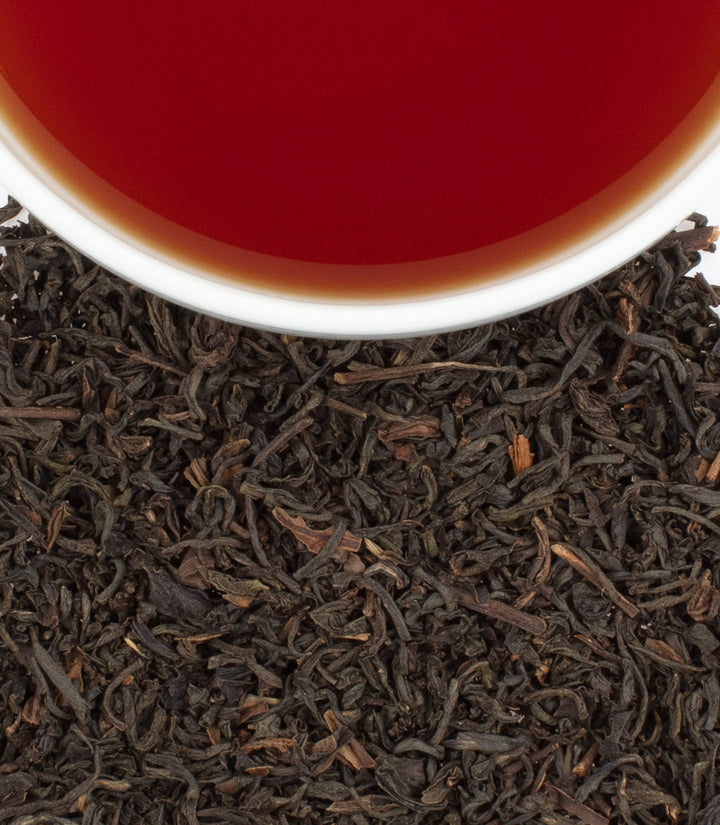 Black tea leaves with a cup of red tea in the background.