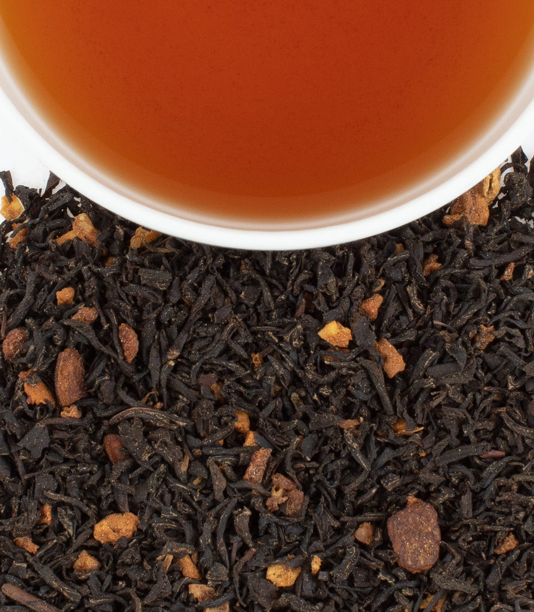 Close-up of black tea leaves with a cup of tea in the background.