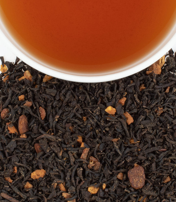 Close-up of black tea leaves with a cup of tea in the background.