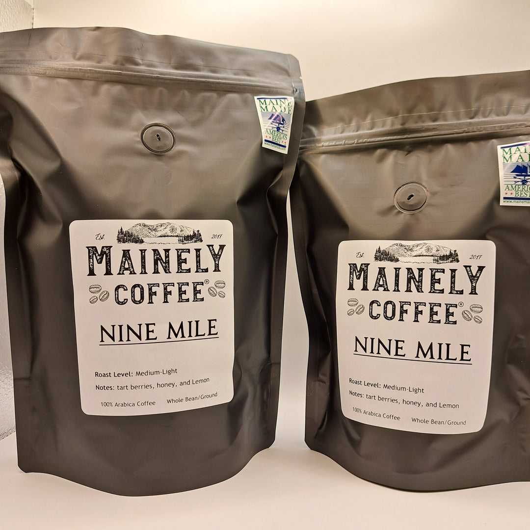 Two brown coffee bags labeled Mainely Coffee Nine Mile on a light background