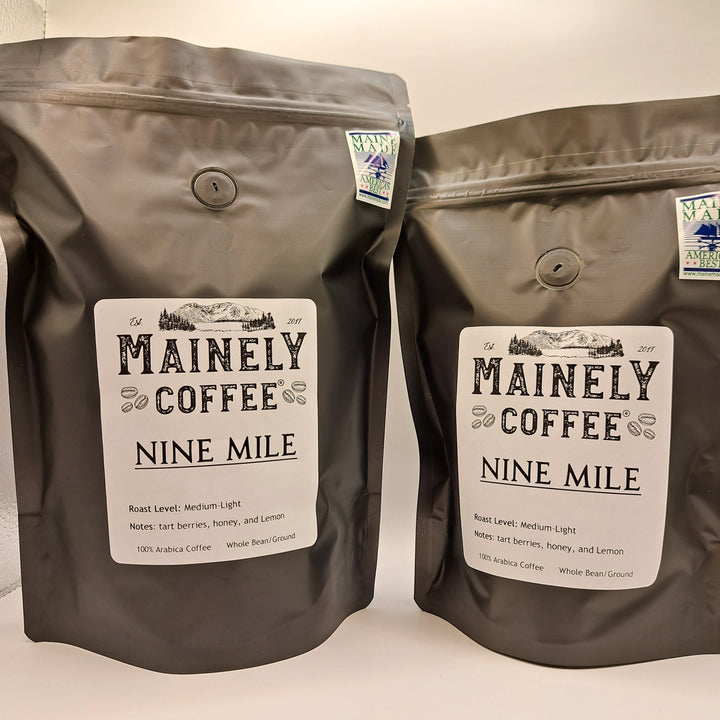 Two brown coffee bags labeled Mainely Coffee Nine Mile on a light background