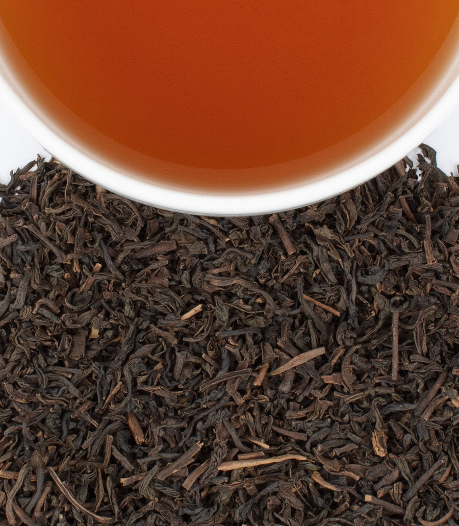 Close-up of tea leaves with a cup of tea in the background.