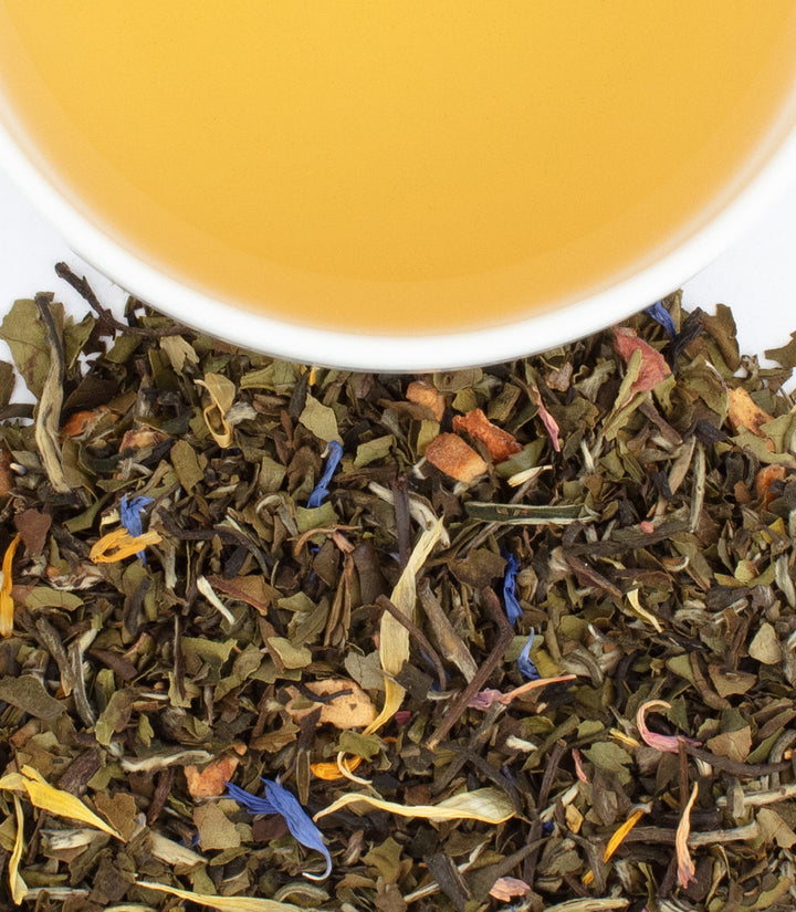 Tea leaves with a cup of tea in the background.