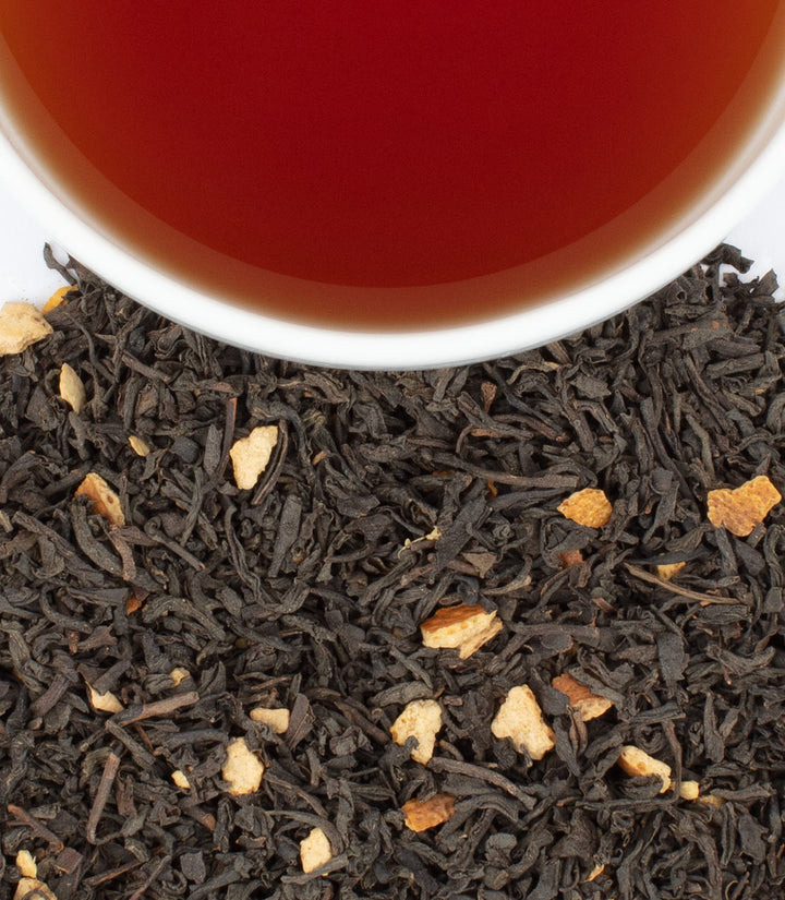 Tea leaves with a cup of tea in the background.