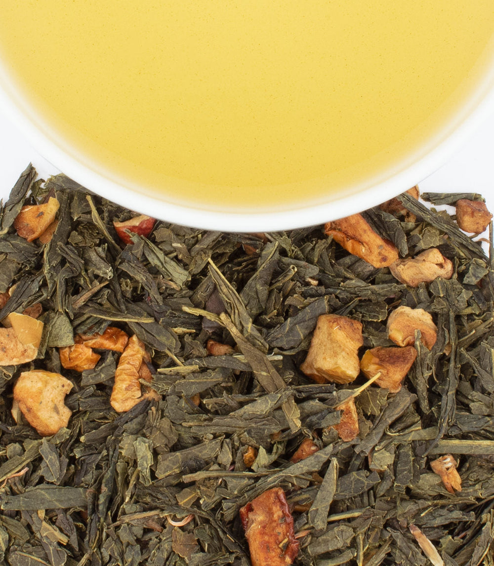 Tea leaves with orange pieces and a cup of tea in the background.