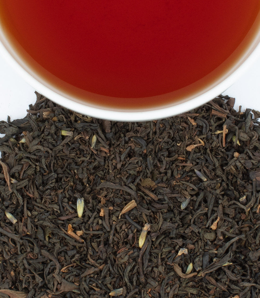 Black tea leaves with a cup of tea in the background