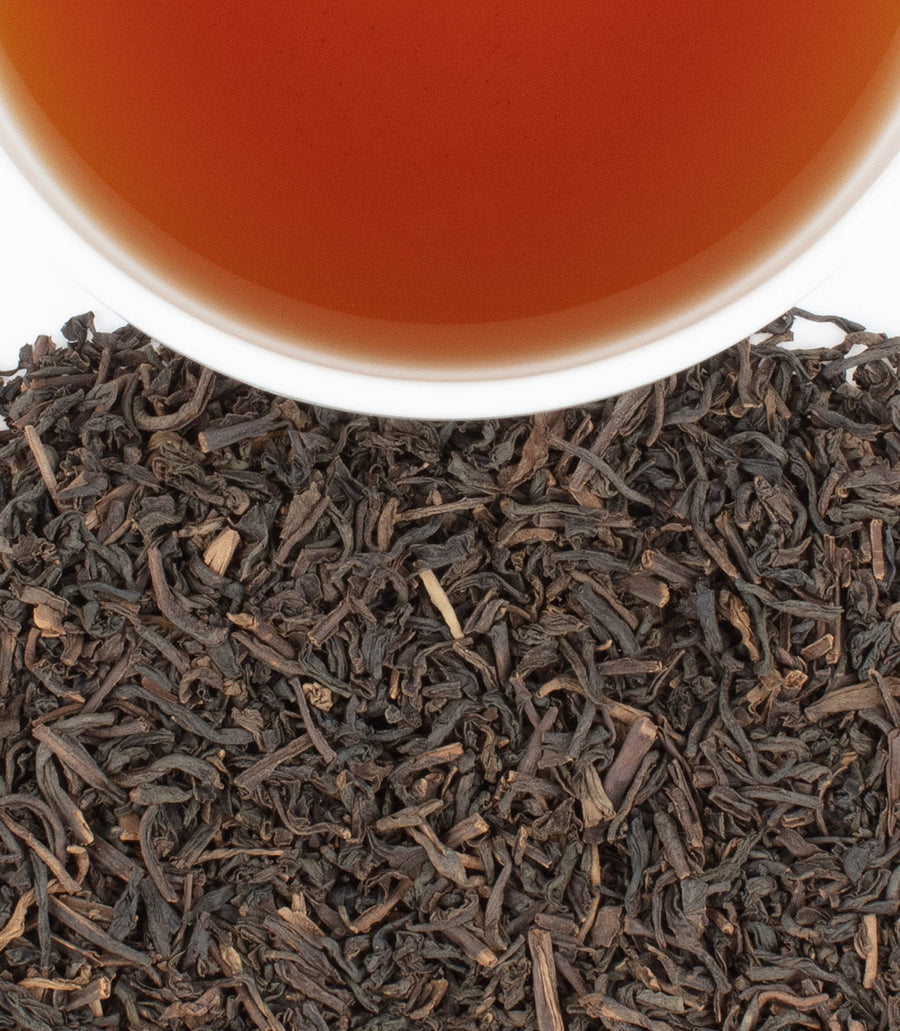 Close-up of black tea leaves with a cup of tea in the background.