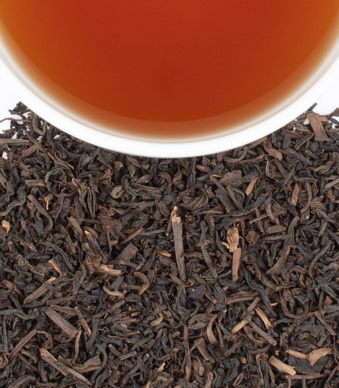 Close-up of black tea leaves with a cup of tea in the background.
