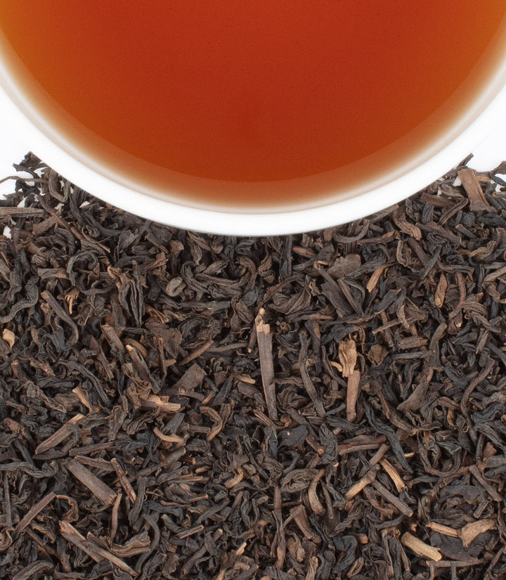 Close-up of black tea leaves with a cup of tea in the background.