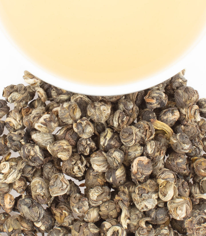 Close-up of dried tea leaves with a blurred white container in the background.