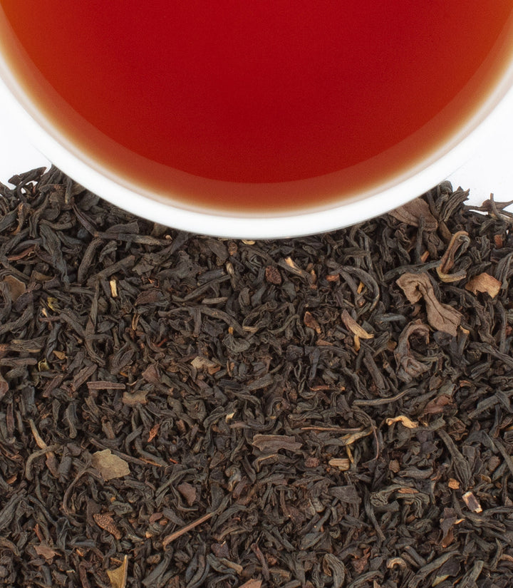 Close-up of tea leaves with a cup of tea in the background.