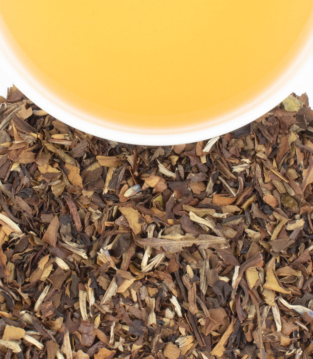 Close-up of dried tea leaves with a cup of tea in the background