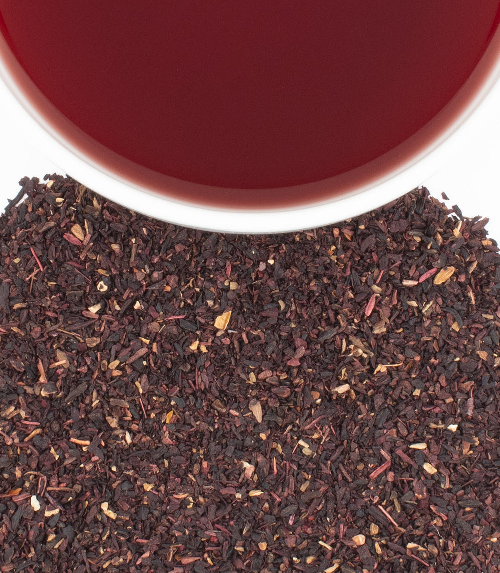 Close-up of dried tea leaves with a cup of red tea in the background