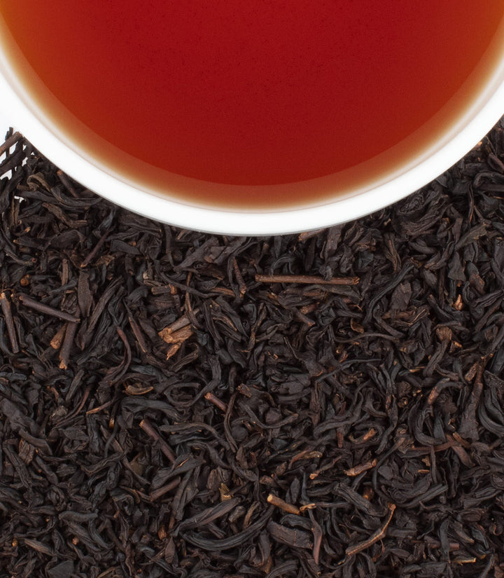 Close-up of tea leaves with a cup of tea in the background.