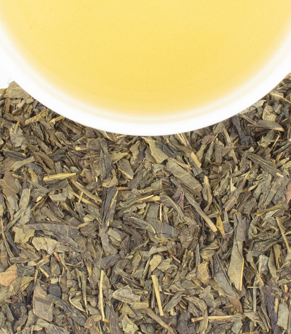 Tea leaves with a cup of tea in the background.
