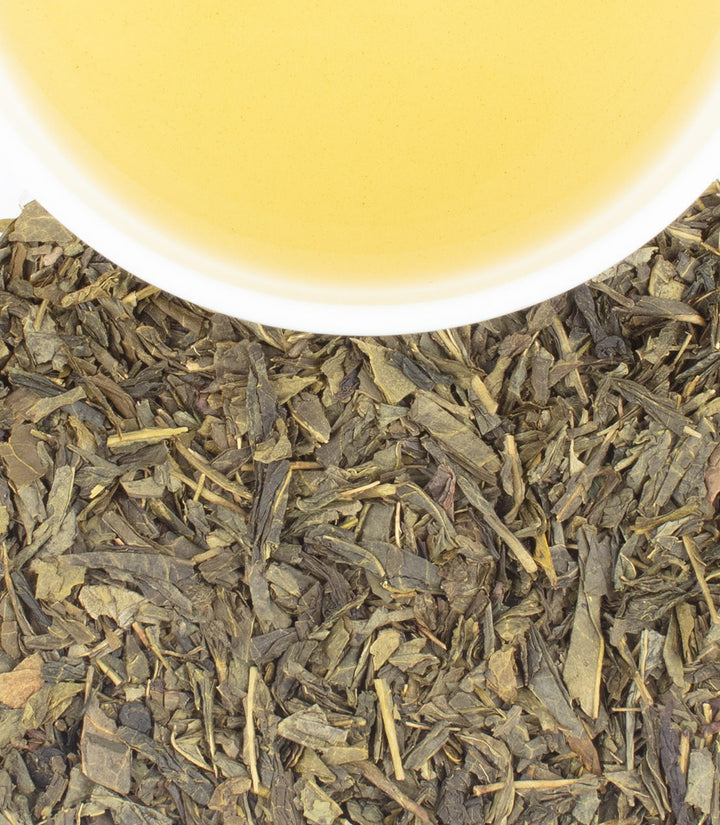 Tea leaves with a cup of tea in the background.