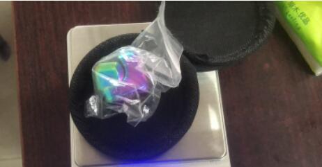 Multicolored gemstone in a clear plastic bag on a white stand with a dark background.