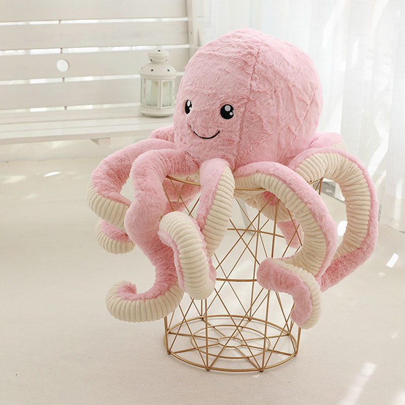 Pink plush octopus toy on a gold wire basket with a white background.