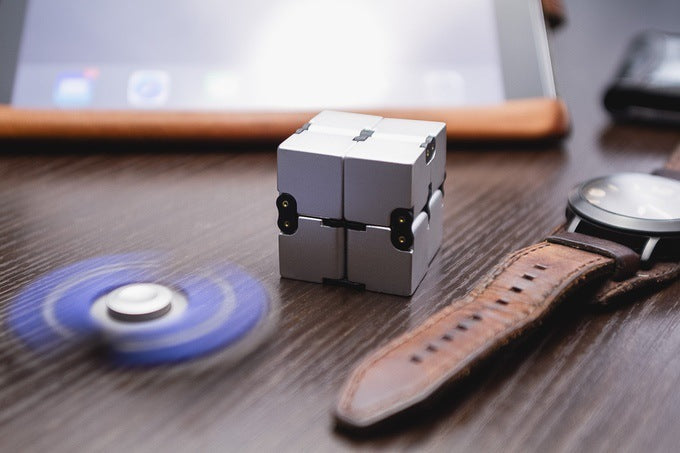 Fidget cube on a desk with a watch and smartphone in the background.