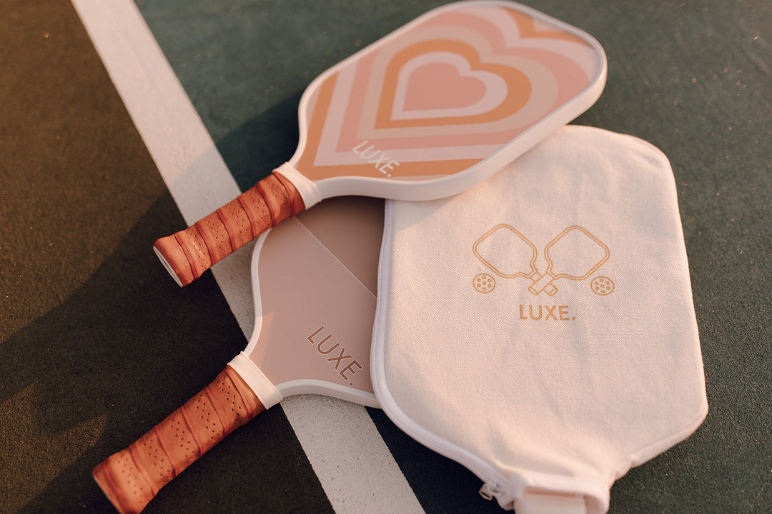Two pink pickleball paddles with wooden handles and a carrying case on a green surface.